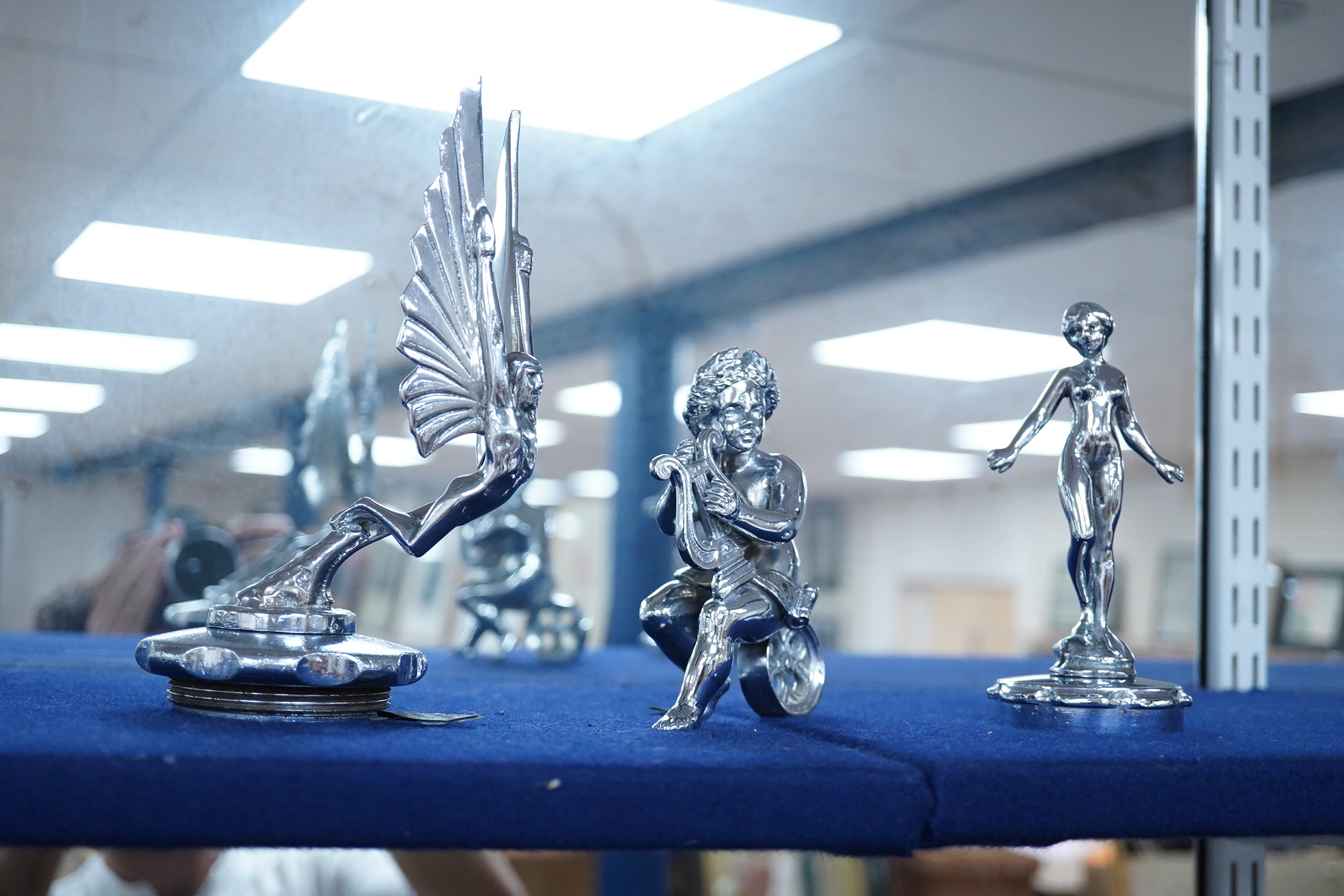Six car mascots including five chrome and brass examples; a female figure, a cherub with harp, an Art Deco winged figure, etc. and a cold painted spelter figure of a skier